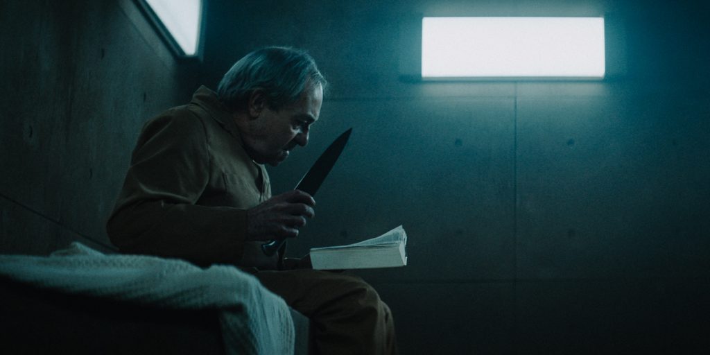"El hoyo", de Galder Gaztelu-Urrutia: La elocuencia del hambre Hombre en celda subterránea sostiene plato de comida frente a ventana luminosa en escena de tensión y privación