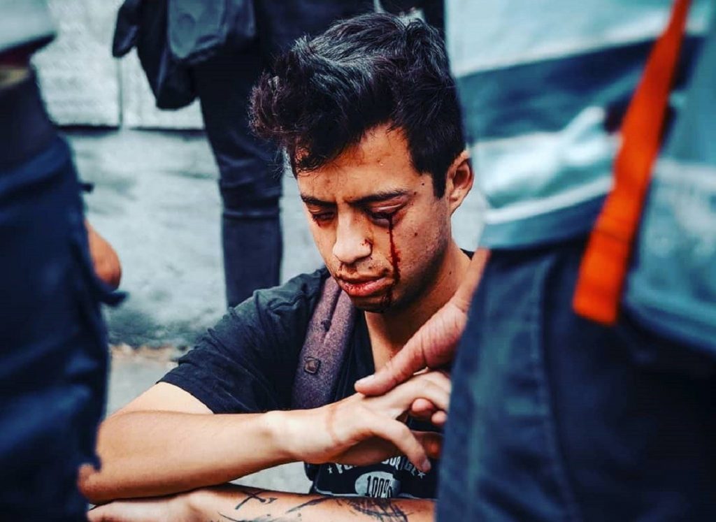 Joven concentrado sosteniendo una cámara de cine, rodeado de equipo técnico azul en set de producción