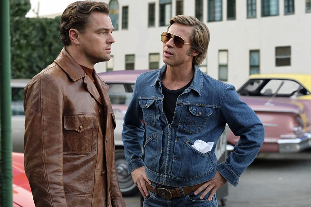 "Había una vez en... Hollywood": Una radiografía al mundillo del cine (o por qué insisto en que el Oscar debió ser para Di Caprio) Dos hombres en un estacionamiento de los años sesenta, uno con chamarra marrón y otro con denim azul y gafas de sol