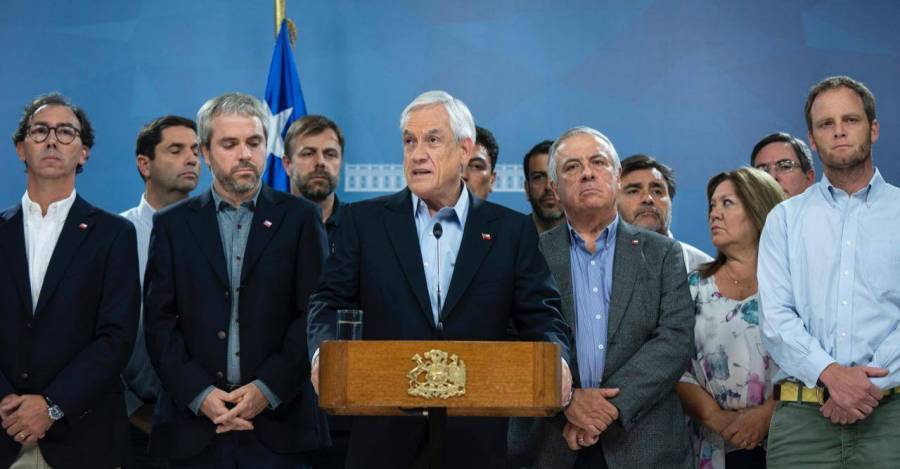 Sebastián Piñera en conferencia de prensa rodeado de ministros y colaboradores, con atril presidencial