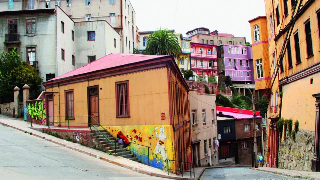 Calle empinada en barrio bohemio con casas de colores vibrantes, edificios históricos y murales, evocando atmósfera