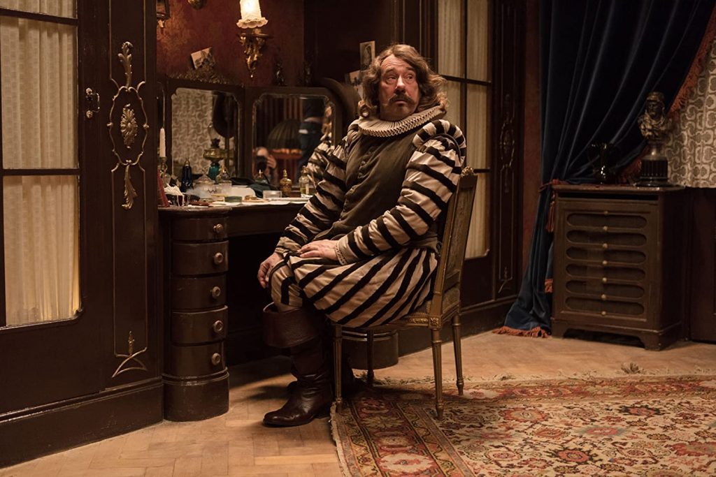 "Cyrano Mon Amour": La apuesta cinematográfica de Providencia para estos días de pandemia Hombre sentado en silla girando hacia la cámara en estudio decorado con espejos y muebles antiguos, vistiendo suéter