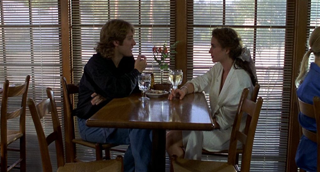 "Sexo, mentiras y videos", de Steven Soderbergh: El aprendizaje del amor Dos personas sentadas frente a frente en una mesa de madera, con ventanas de persiana al fondo, en una escena