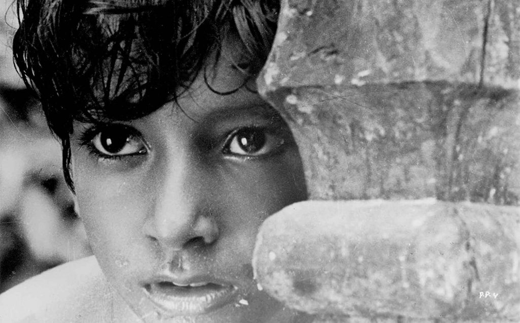 Niño bengalí con expresión pensativa mirando a la cámara, rodeado de textura de ladrillo en blanco y negro