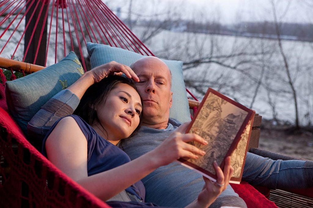 Pareja en hamaca leyendo libro juntos al atardecer junto a un lago con bosque al fondo