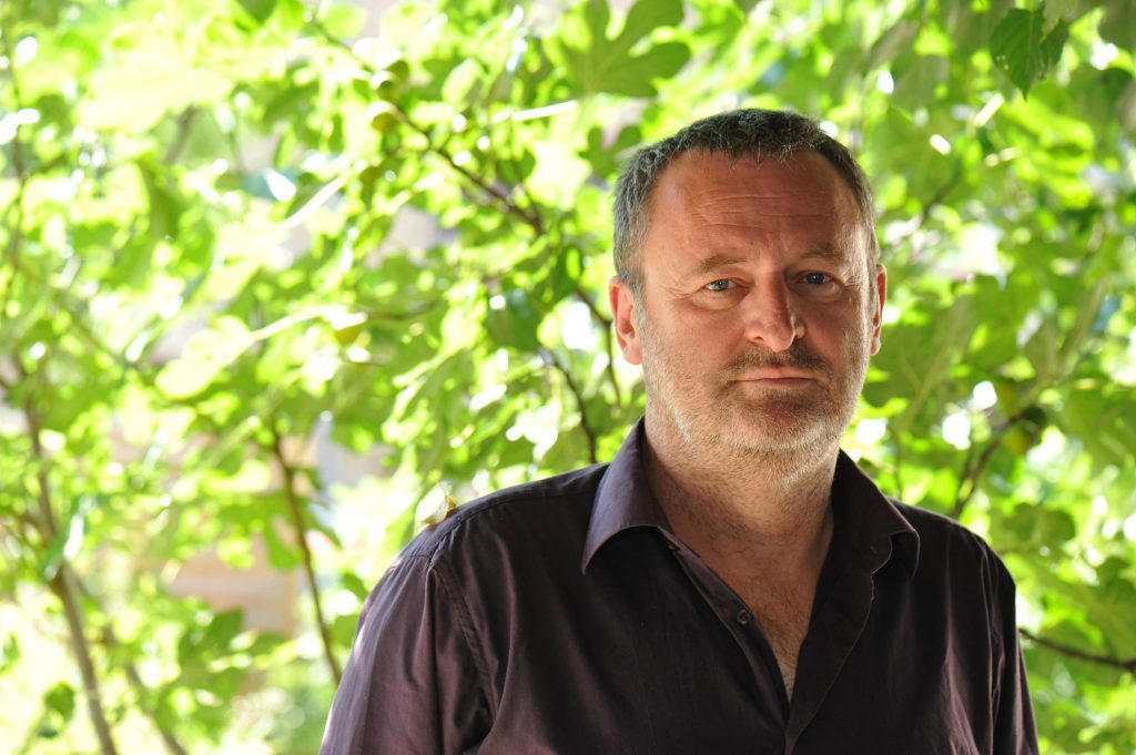 Velibor Čolić, escritor bosnio, retrato de perfil tres cuartos contra fondo de vegetación verde