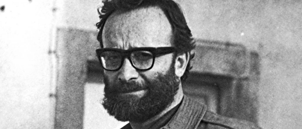 Hombre de mediana edad con gafas y barba, vistiendo suéter de cuello alto, en fotografía en blanco y negro