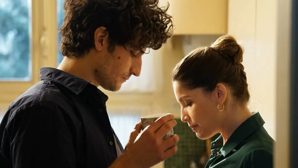 Dos personas en una cocina, él de perfil sosteniendo su mano, ella mirando hacia abajo en momento íntimo de la película