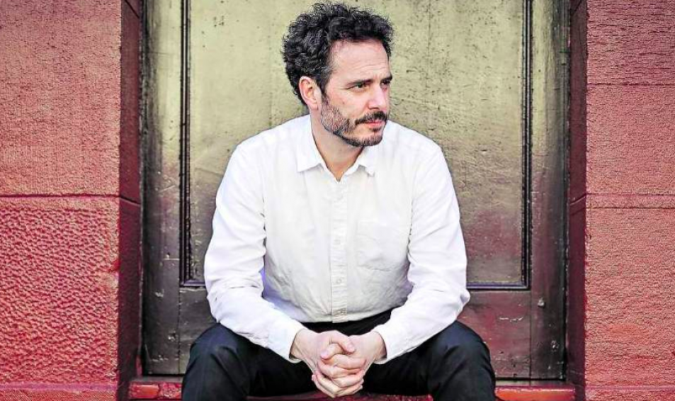 El lugar sin límites: La ética de la "cultura Evopoliana" Hernán Larraín Matte sentado contra pared de ladrillo rojo, camisa blanca, mirando hacia el lado izquierdo