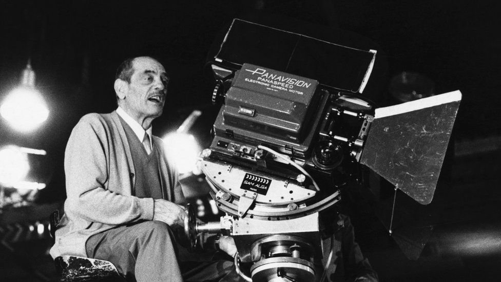 Luis Buñuel junto a una cámara de cine en plano medio, durante el rodaje de una película en blanco y negro