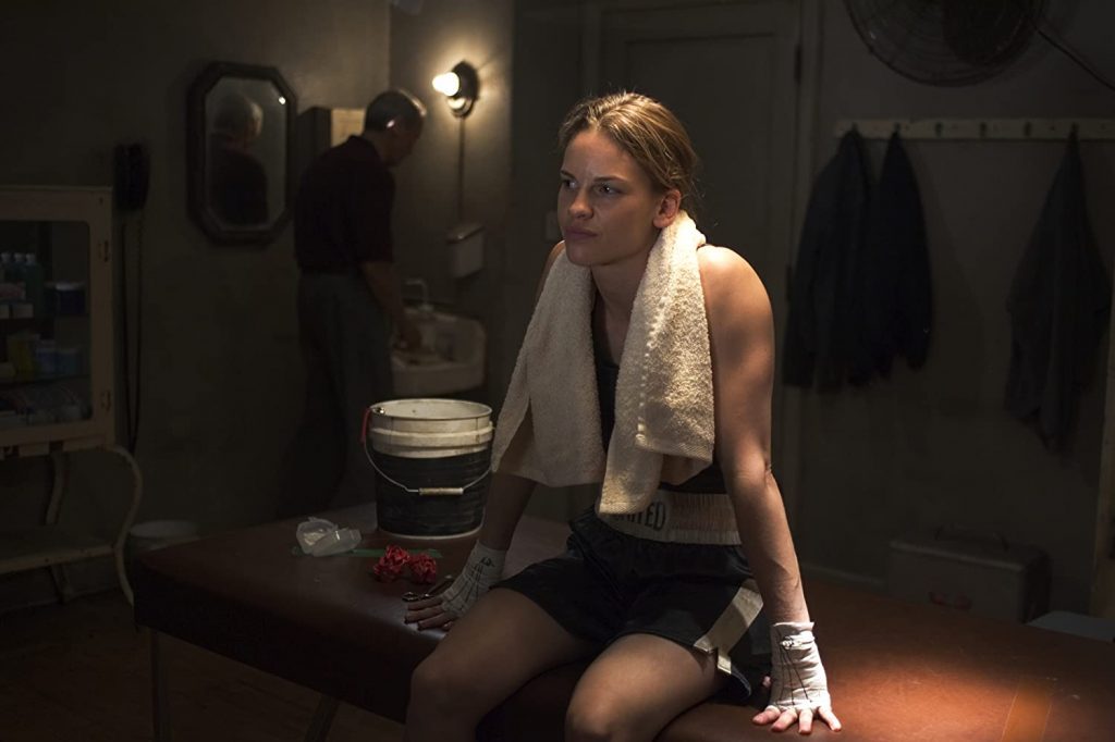 Los 90 años de Clint Eastwood: "Million Dollar Baby", el sueño americano con rostro de mujer Mujer en cuarto oscuro frente a espejo con toalla al cuello, escena de drama cinematográfico con iluminación tenue
