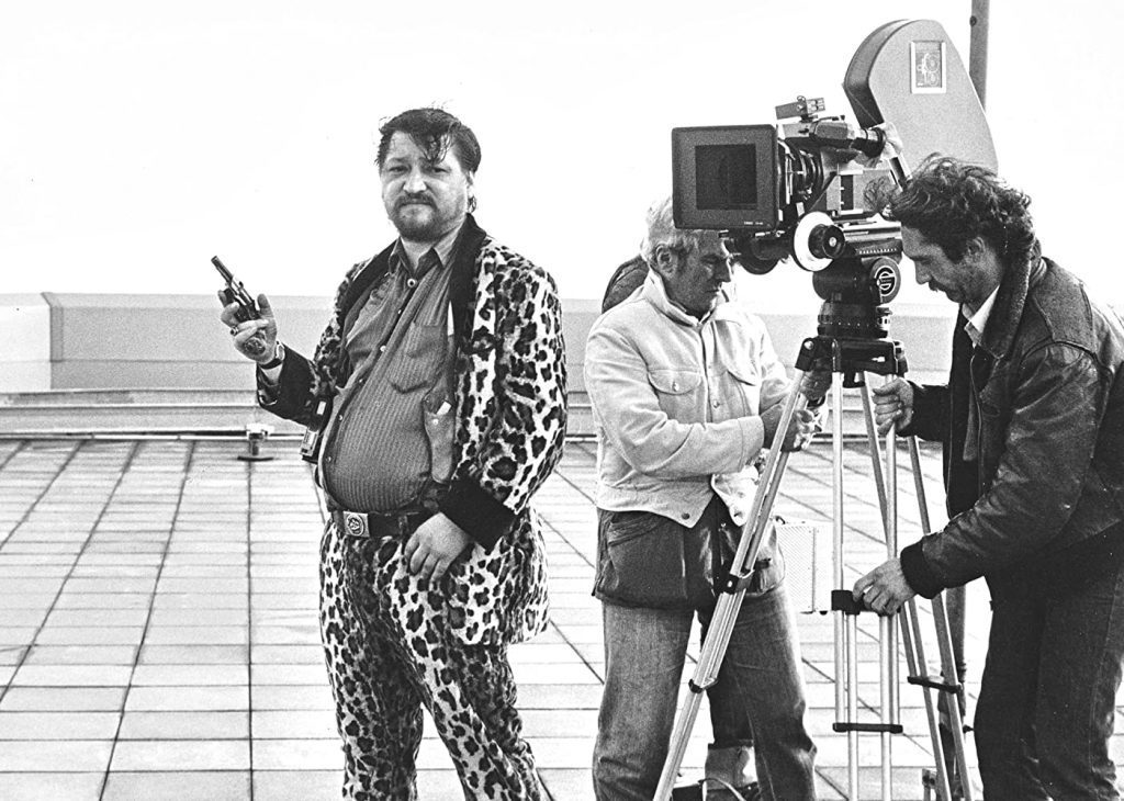 Rainer Werner Fassbinder en chaqueta de leopardo con micrófono durante rodaje, rodeado de equipo técnico de cine
