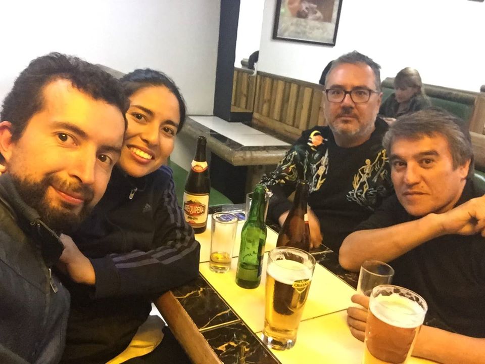 Cuatro personas brindando con botellas de cerveza alrededor de una mesa en ambiente informal