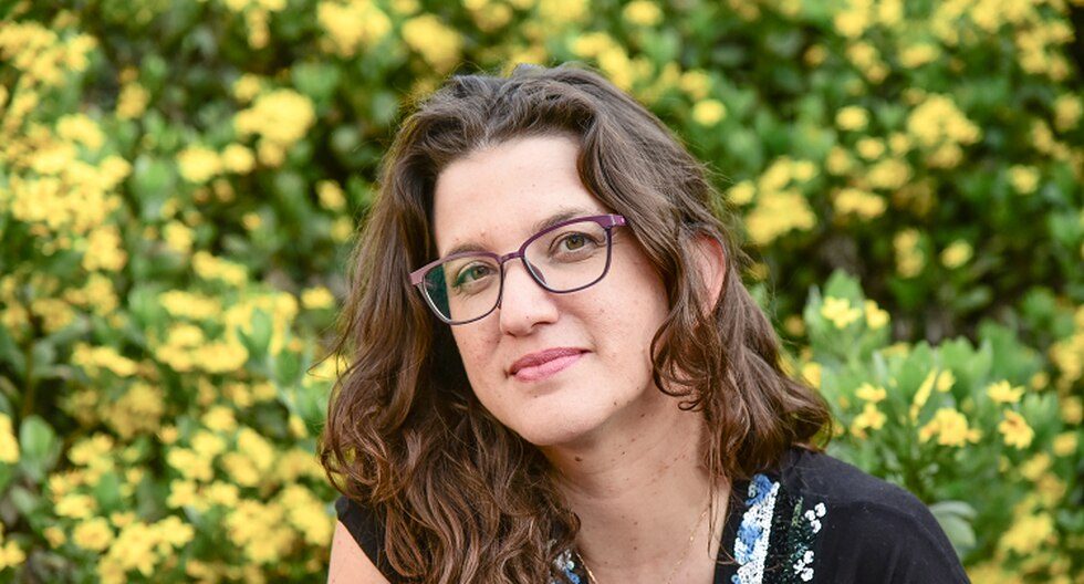 María José Navia, autora, con gafas y cabello ondulado castaño, frente a fondo de flores amarillas