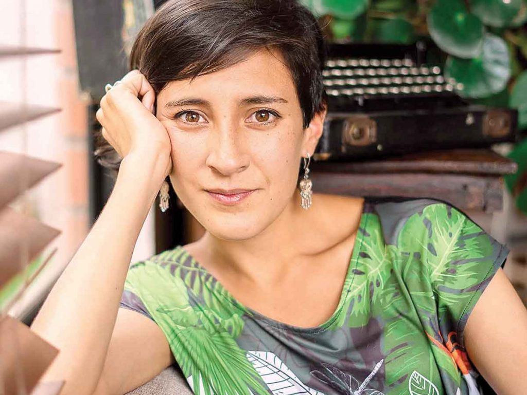 Natalia García Freire, escritora ecuatoriana, posando con la mano cerca del rostro frente a fondo verde
