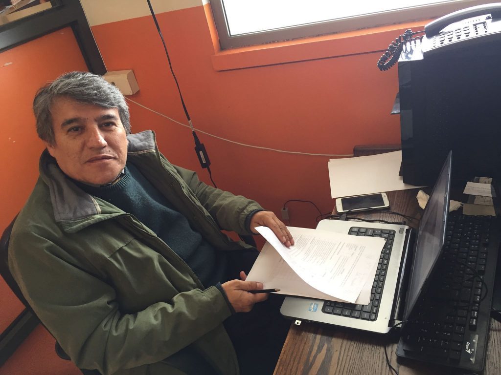 Hombre sostiene carpeta con documentos en estudio radiofónico con pared naranja de fondo
