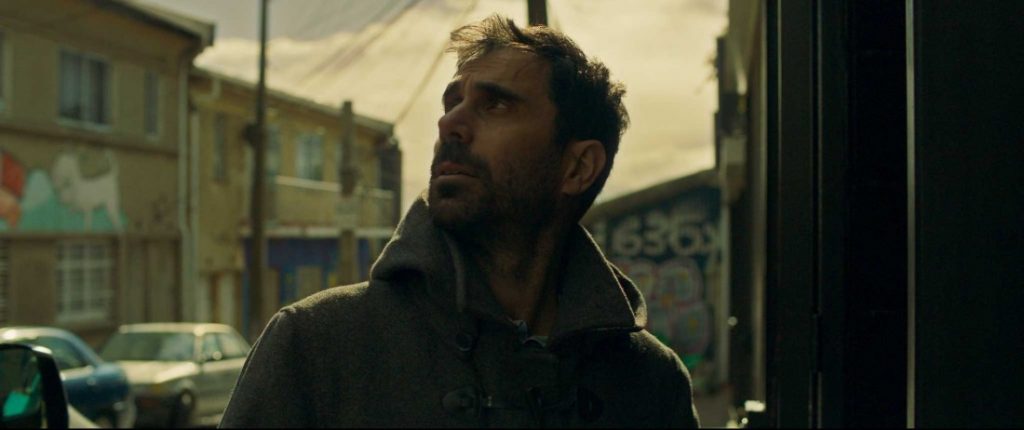 SANFIC 16: "De la noche a la mañana", La inestabilidad del "yo" en la hipermodernidad Hombre con barba en entorno urbano, mirada pensativa, escena que sugiere introspección y conflicto interior en contexto