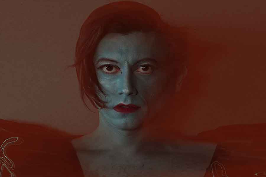 Retrato artístico de mujer con tonalidades rojizas, mirada frontal intensa y cabello largo rojo oscuro sobre fondo