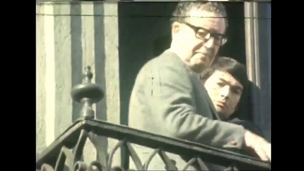 Hombre mayor con anteojos sosteniendo a un niño pequeño en una ventana con barandilla de hierro