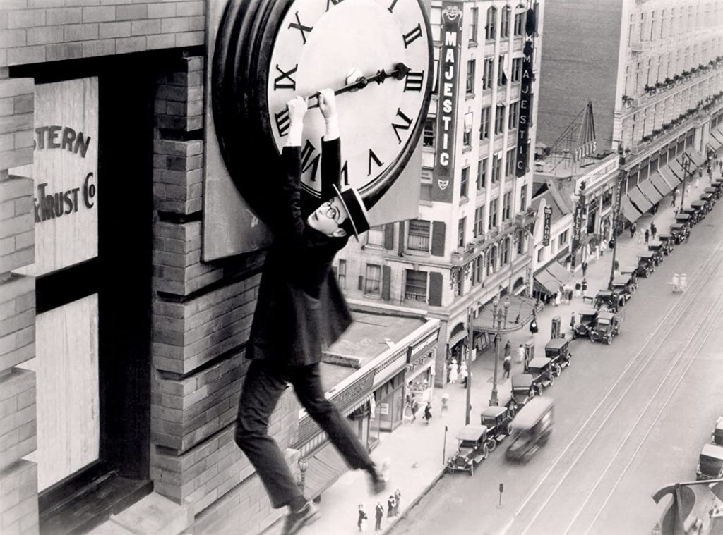 Harold Lloyd cuelga de un reloj gigante en la fachada de un rascacielos mientras la ciudad se ve abajo