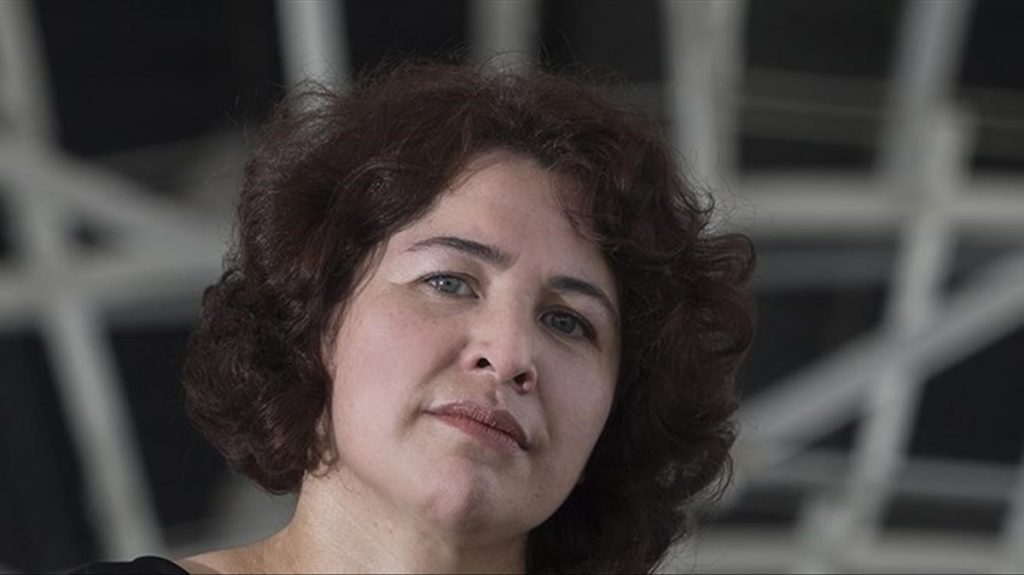 Claudia Hernández, escritora salvadoreña, con expresión contemplativa y cabello rizado, sobre fondo desenfocado