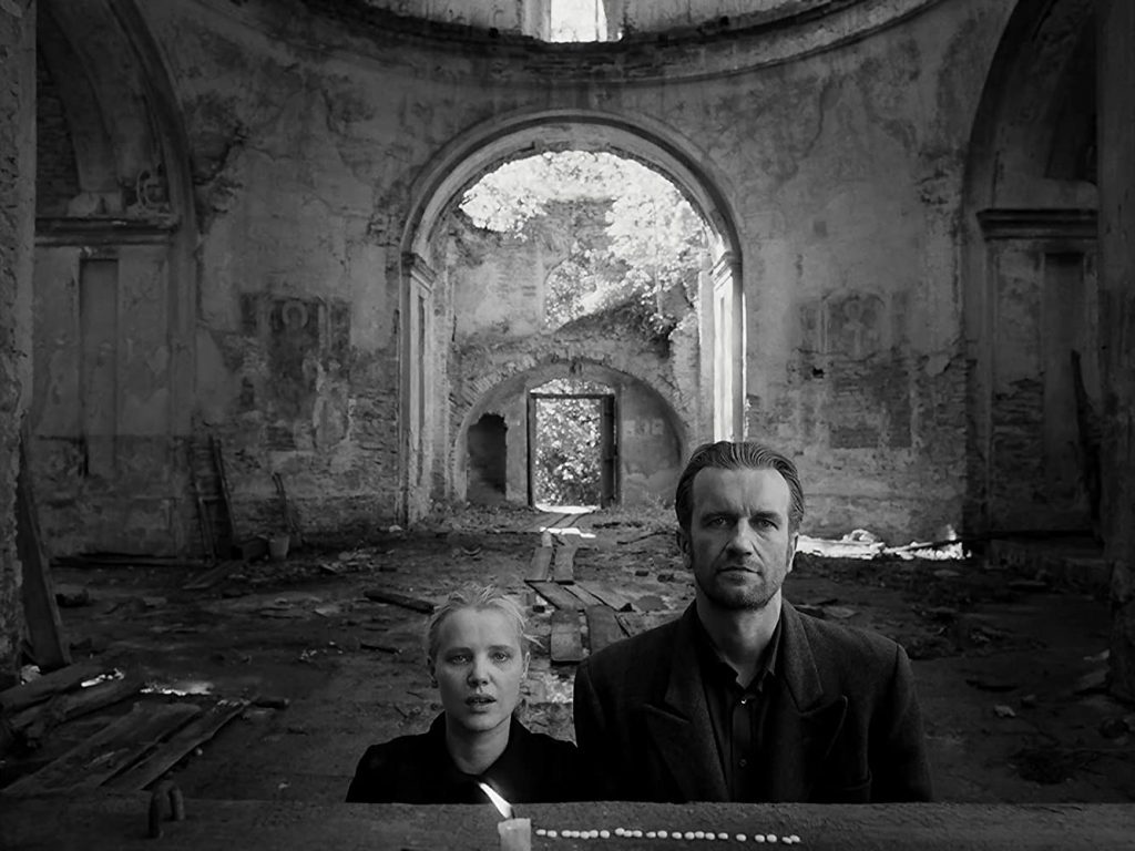 "Cold War": Un amor sin tiempo ni lugar Hombre y mujer jóvenes en ruinas de edificio con arco de piedra al fondo, fotografía en blanco y negro