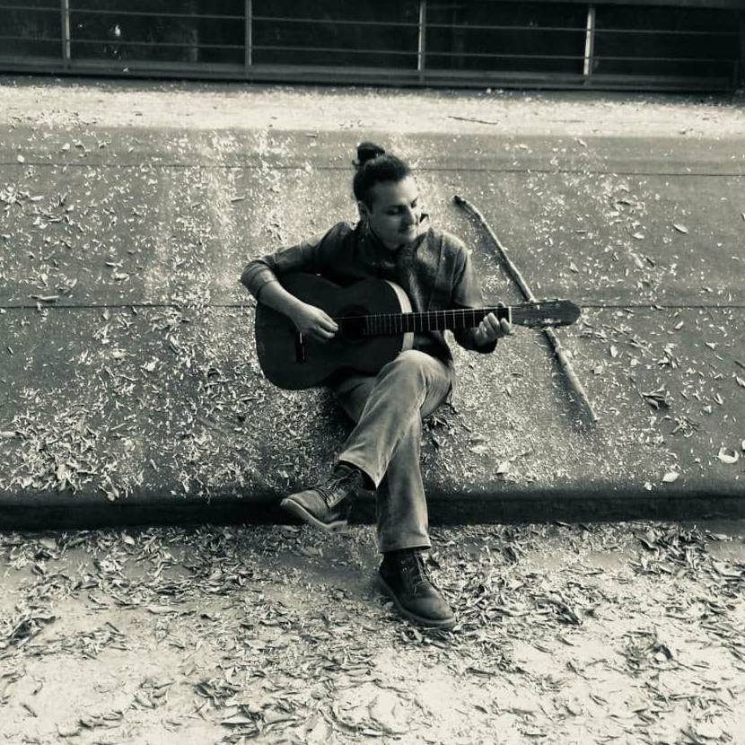 Andrés Cisnegro con guitarra sentado en tierra, fotografía en blanco y negro de perfil