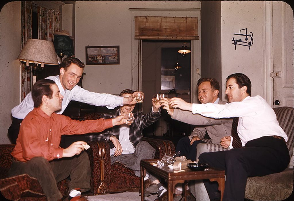 Cuatro hombres en traje realizan un brindis en una sala, años 60, ambiente de celebración política
