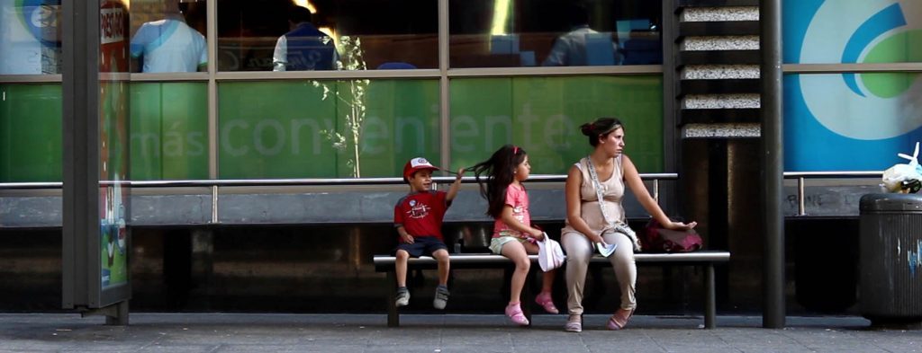 Cinco personas sentadas en una banca urbana frente a un escaparate verde, esperando en la calle