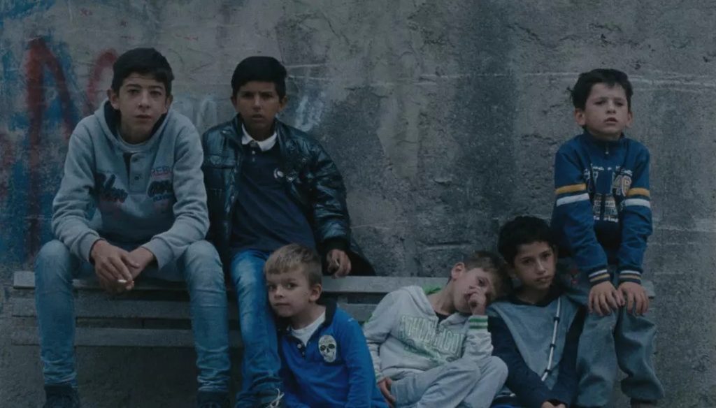 "La ciambra": El patio trasero de Europa Grupo de niños sentados contra pared gris en escena de drama social sobre infancia vulnerable en Europa del Este