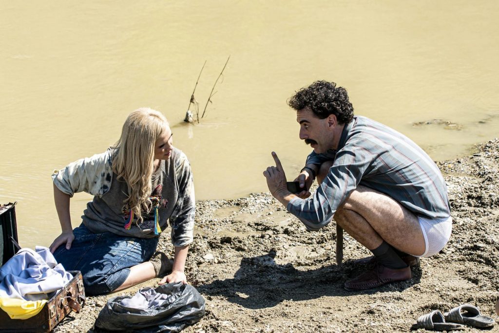 Dos personas excavando en la arena cerca del agua, buscando algo con herramientas improvisadas