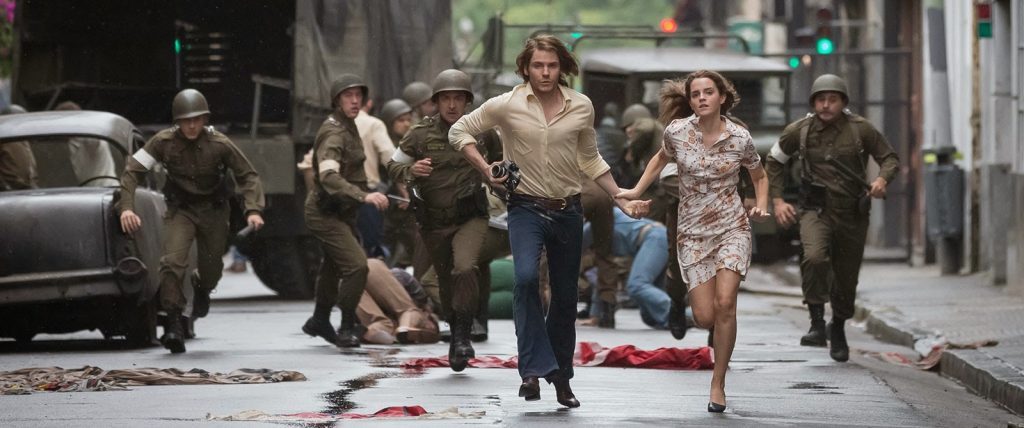 Grupo de personas corriendo en calle urbana, algunos en ropa militar y civil, escena de tensión y huida