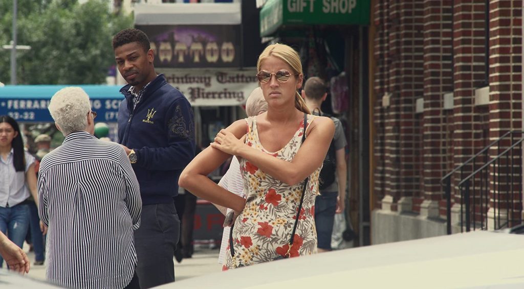 Mujer con vestido floral y gafas de sol en calle de Nueva York, junto a transeúntes en escena urbana