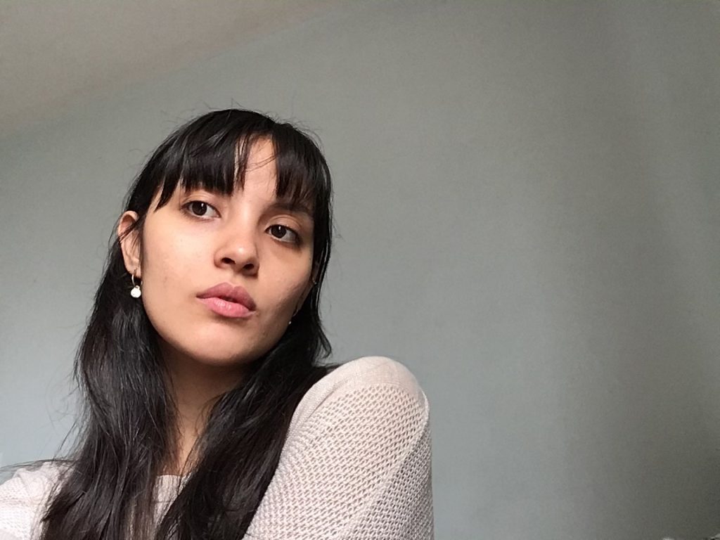 "Quisiera que oyeran la canción que escucho cuando escribo esto": Una novela de aprendizaje femenino Mujer joven de cabello largo negro y flequillo, mirando hacia arriba, vistiendo blusa clara de textura puntillada