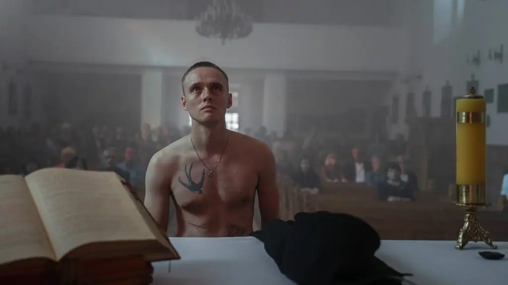 Hombre sin camisa en iglesia, junto a libro abierto y vela, con congregación de fondo