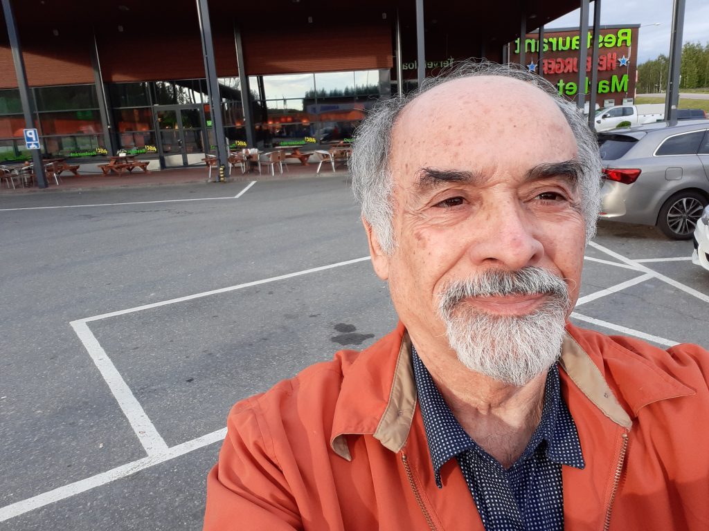 Juan Mihovilovich, escritor chileno, en selfie al aire libre frente a estacionamiento y comercios