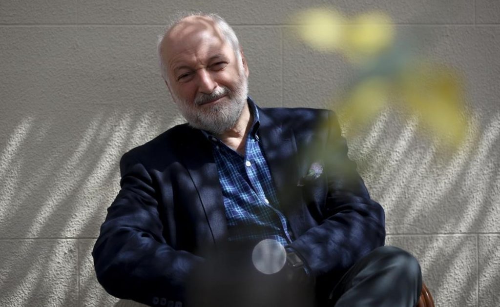 André Aciman, autor estadounidense de origen egipcio, sonríe en primer plano con fondo desenfocado