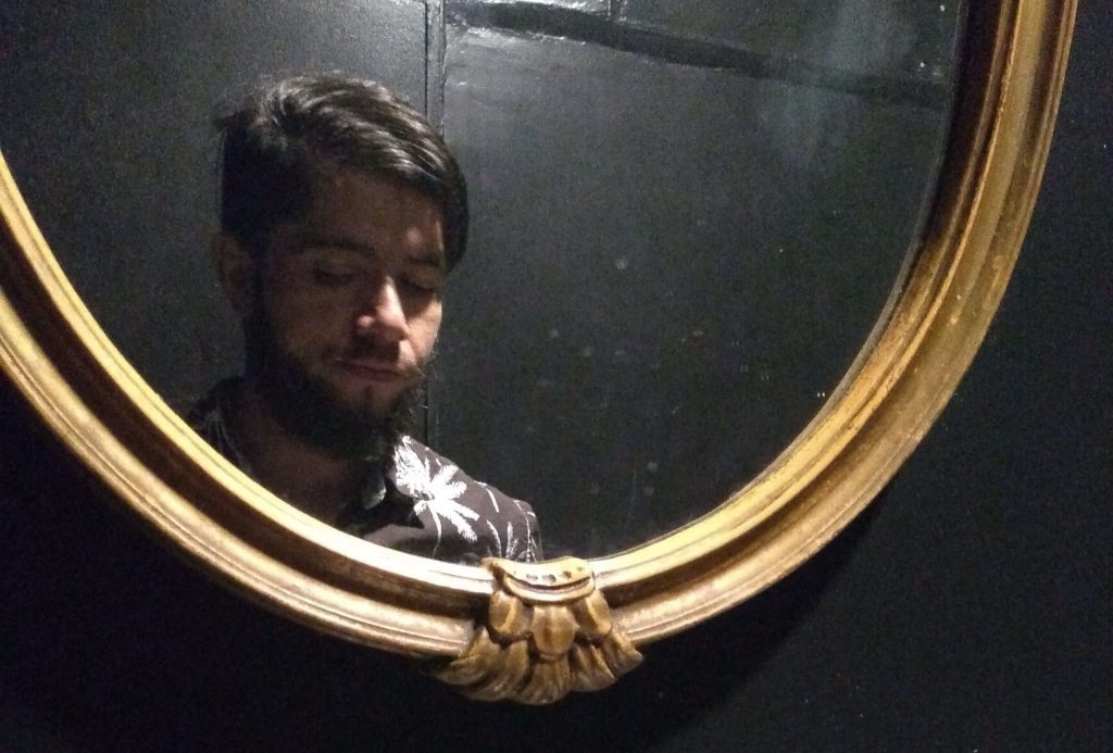 Gastón Carrasco Aguilar reflejado en espejo dorado con marco ornamental, ambiente oscuro