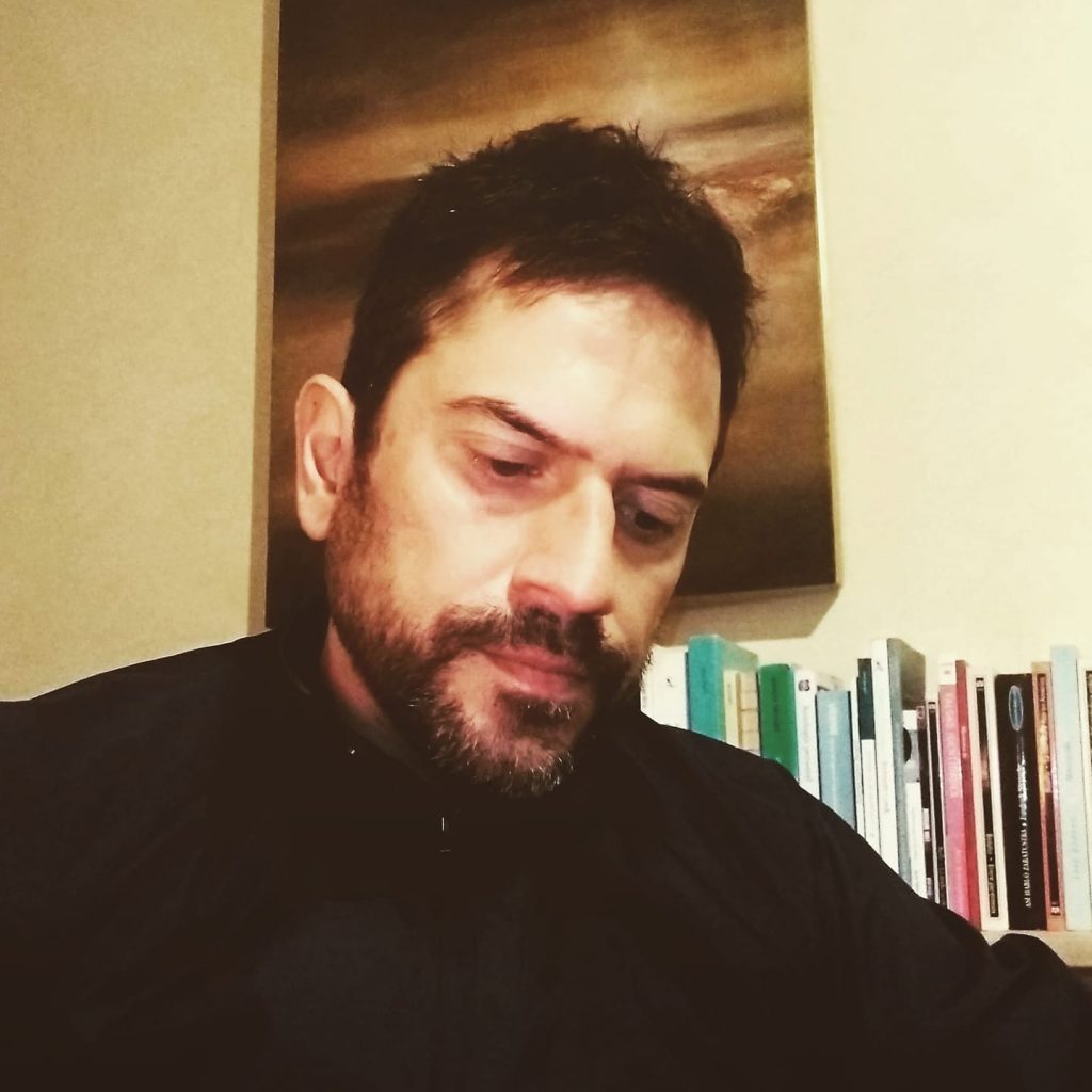 Ignacio Borel, hombre con barba oscura y cabello negro, mirando hacia abajo en interior con estantería de libros