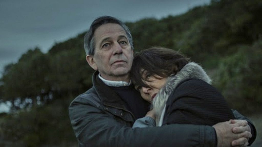 Hombre de mediana edad sostiene a una niña pequeña contra su pecho en un bosque oscuro y lluvioso