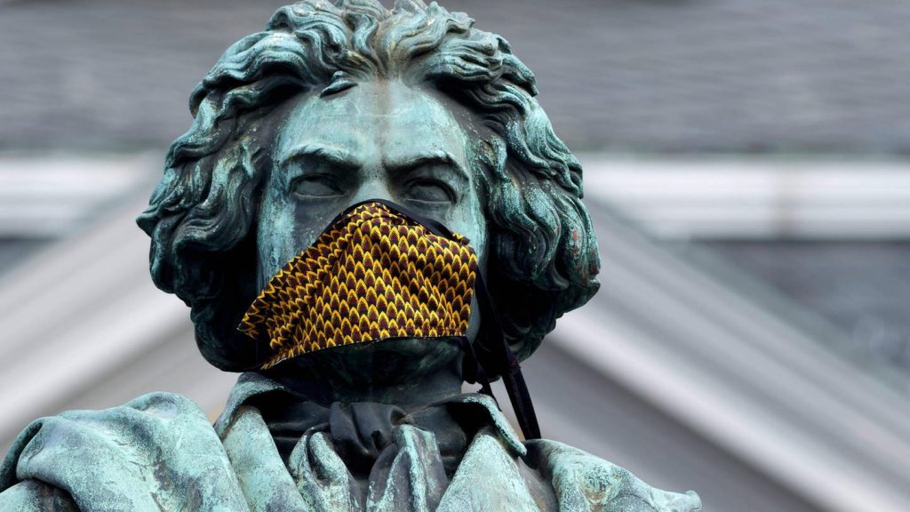 Estatua de Beethoven con la boca cubierta por una máscara dorada en primer plano, simbolizando censura o silenciamiento