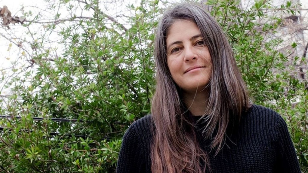 Selva Almada, escritora argentina, retratada de frente con cabello largo castaño ante fondo de vegetación verde