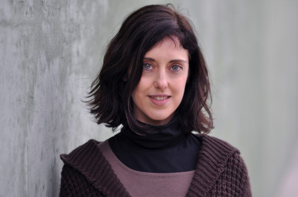 Irene Vallejo, autora de El infinito en un junco, posa frente a fondo gris con suéter marrón