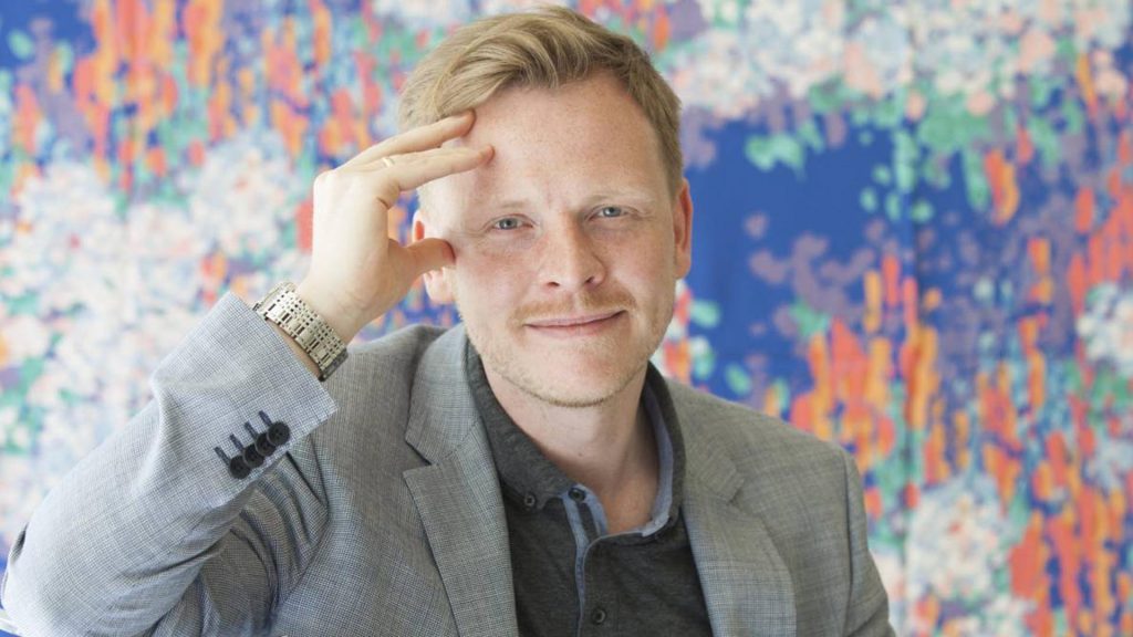 Markus Gabriel, filósofo alemán, apoya su cabeza con la mano frente a mural colorido con formas abstractas