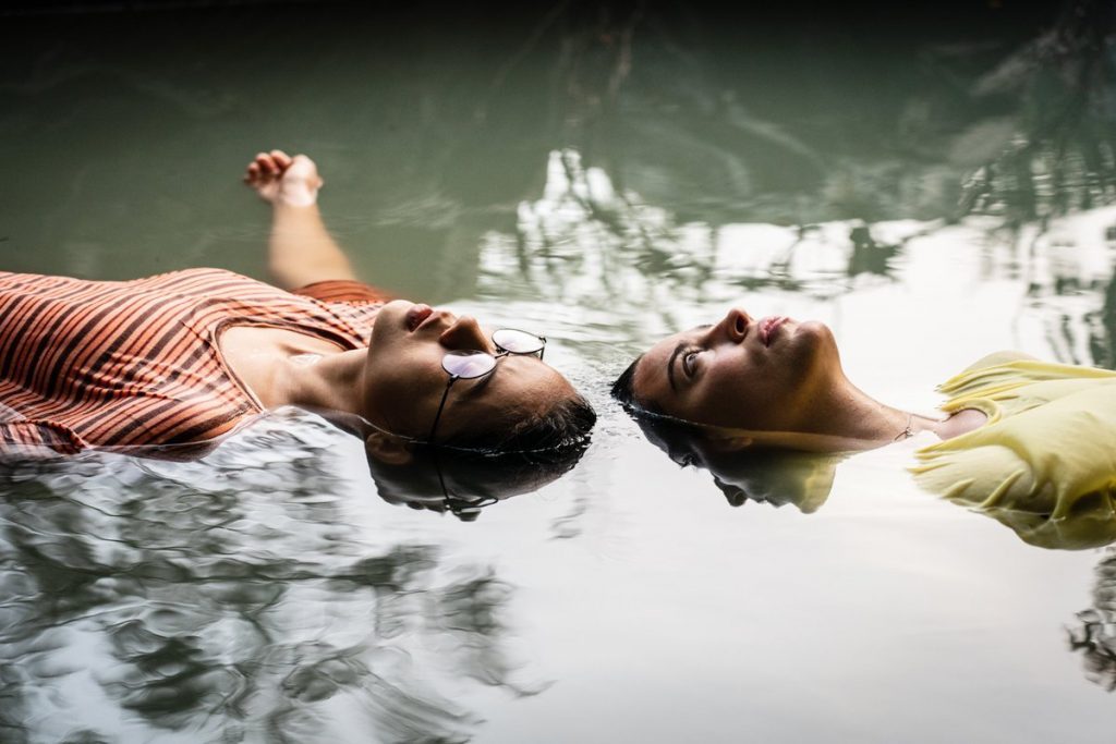 Dos personas recostadas en agua reflejando sus rostros, escena de intimidad emocional y conexión romántica