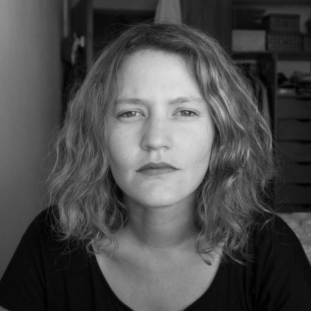 Retrato en blanco y negro de Carolina Brown, mujer de cabello ondulado largo, mirando a la cámara con expresión seria