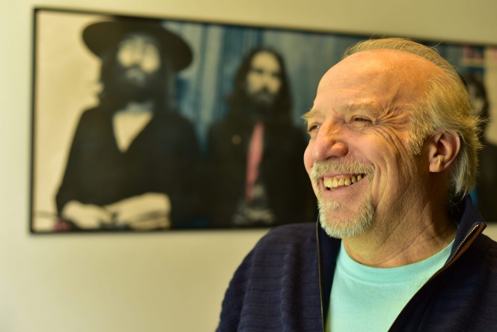 Antonio Ostornol sonríe de perfil mientras observa hacia la derecha, con cuadros de arte al fondo