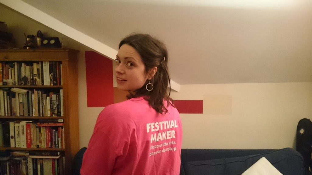 Lizzy de perfil vistiendo camiseta rosa, en interior con estantería de libros al fondo