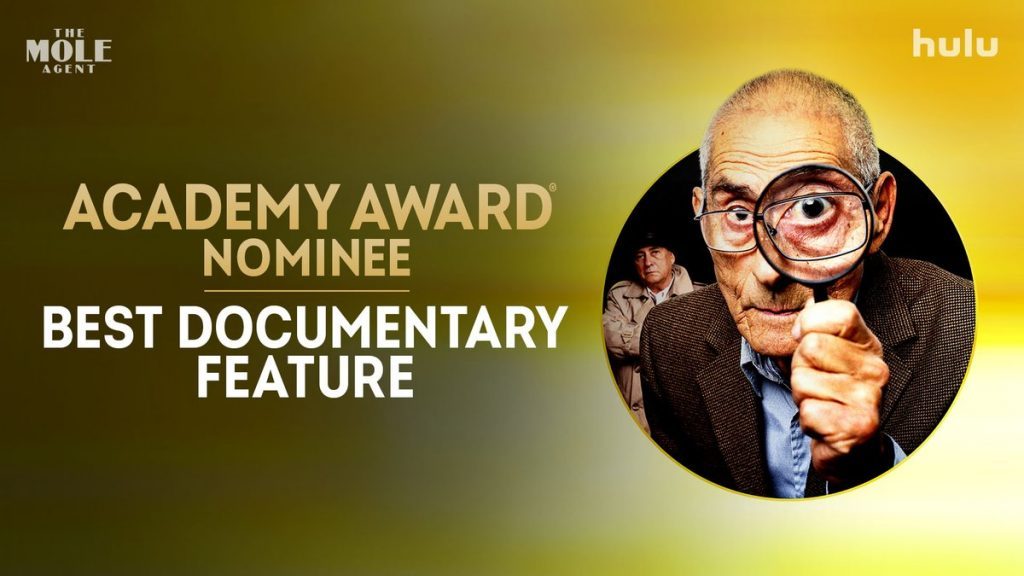 Hombre mayor con gafas señalando hacia la cámara, fondo dorado con logo de Hulu, texto nominación Academy Award Best