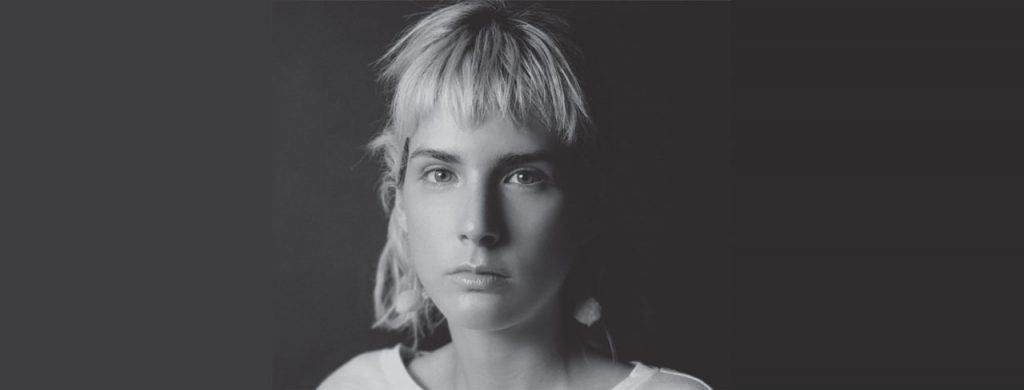 Paulina Flores, escritora chilena, retrato en blanco y negro con fondo gris neutro, mirando hacia la cámara